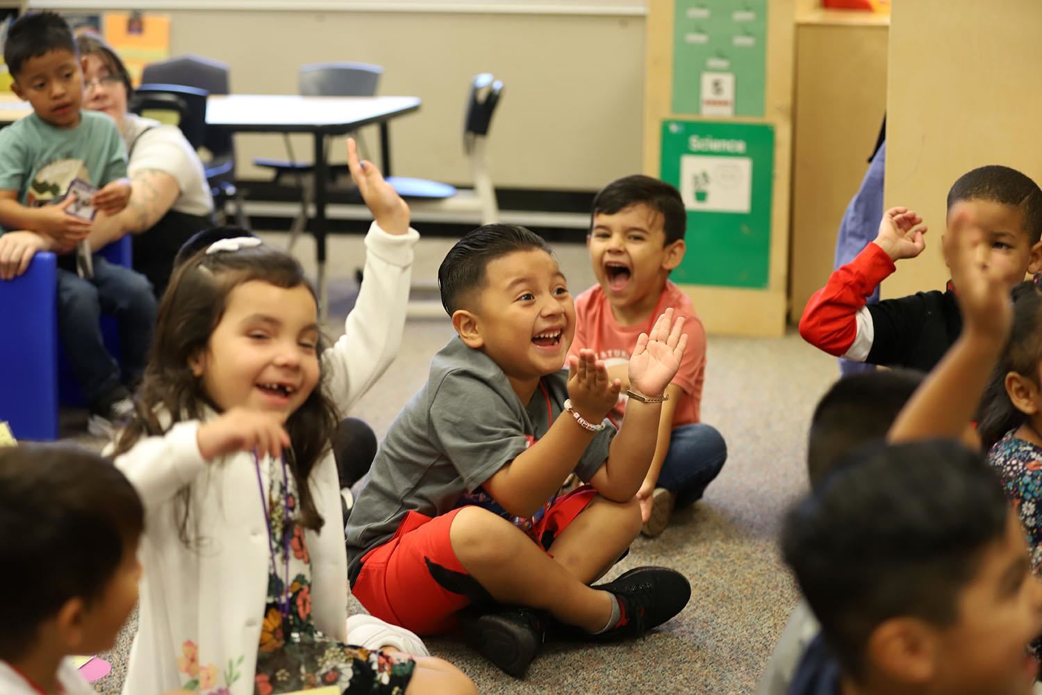 Smiling and clapping Kindergarten students at Howard Elementary sitting on the floor for group time.